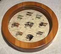Top view showing the round shadow box with nine fishing flies mounted on birch bark.