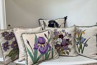 Five decorative needlepoint pillows displayed on bench showing various floral motifs