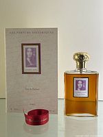 Full lot view: perfume bottle standing next to original box and red ribbon on glass surface