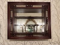 Front view showing full cabinet, carved rosewood frame, glass front door, mirrored back and two glass shelves