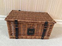 Front view of closed wicker basket on carpet showing leather straps and Harrods plaque