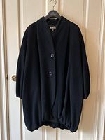 Full front view of black cocoon coat on hanger