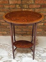 Front view of the oval table showing tabletop, legs, and lower shelf against a brick background