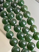 Close-up of polished dark green round jade beads and knotting