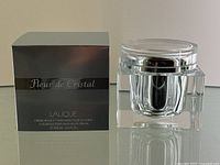 Photo showing the original black box with silver text and the clear acrylic jar of Lalique Fleur de Cristal body cream on a mirrored surface.