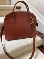 Front view of cognac leather dome handbag with long detachable strap draped