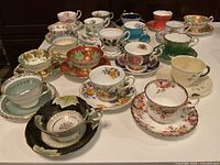 Overview of twenty assorted china cup and saucer pairs arranged on table.