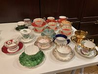 All 19 teacup and saucer sets arranged on table showing variety of patterns and colors