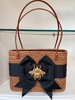 Front view of woven bag with grosgrain ribbon bow and bee hardware