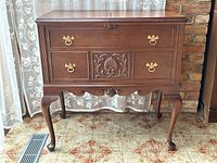 Front view of closed cocktail bar showing carved front and brass hardware