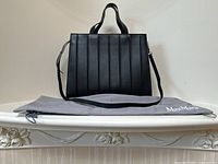 Front view of purse on gray Max Mara dust bag showing vertical stitched panels and attached shoulder strap