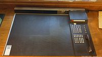 Full top-down view of the desk organizer showing the large black leatherette writing pad and the right side panel with the phone handset and calculator setup.