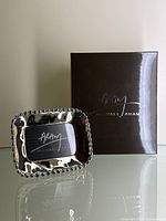 Michael Aram chrome photo frame shown upright with its branded box behind it for identification.