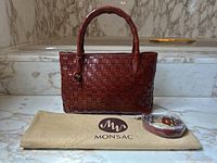 Front view of brown woven leather handbag with dust bag and rolled strap placed in front
