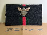 Front view of black beaded clutch with bee motif and green/red bead stripe on front flap