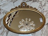 Full view of oval mirror on marble floor showing shape, frame detail, and reflective surface