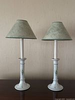Pair of vintage ceramic table lamps standing side by side showing their overall shape, painted base details, and green fabric lampshades.