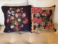 Pair of vintage needlepoint floral pillows on couch, showing front side of both pillows.