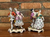 Front view of both porcelain dancing couple figurines on wooden surface