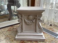 Front angle view of resin pedestal display stand showing scroll work and garland decoration on the side panel.