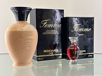 Front view of Rochas Femme glass perfume bottle filled with amber perfume, next to a frosted glass 200ml body lotion bottle with black and gold original packaging boxes behind.