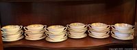 Twelve white porcelain cream soup bowls and matching underplates arranged in two rows on wooden shelf