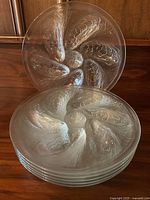 Front view of all six clear glass oyster plates stacked with one plate propped behind to show design