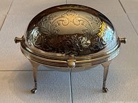Full view of silver plated tureen with domed embossed lid, standing on four legs with paw feet