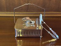 Front angle showing closed sardine dish with fish finial on lid and fish-shaped tongs resting against it