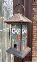 Front view of bird feeder showing stained glass panels, feeding port and metal frame