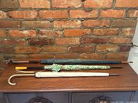 All three umbrellas laid side by side on table against brick wall