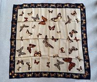 Full view of the square silk scarf featuring cream-colored center with multiple butterfly illustrations and a black border decorated with butterfly motifs.