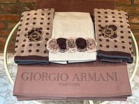 Five towels laid out: two brown Giorgio Armani Parfums bath towels at bottom and three Ungaro hand towels (two polka dot, one with floral trim) on top