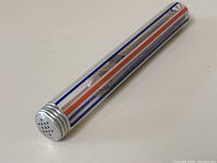 Art glass cigar tube lying on a flat surface showing metal lid and colorful stripes on the glass tube body.
