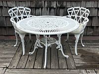 Round white cast aluminum table with radial top and two matching chairs on wooden deck.