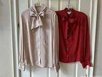 Two vintage Celine pussy bow blouses (cream and red) hanging on door