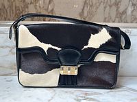 Front view of bag showing black and white hair-on cowhide panels, black leather trim, and gold-tone push-lock clasp