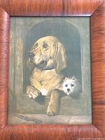 Close-up of print showing two dogs, a large tan dog and smaller white dog, in a stone window setting inside a wood frame.
