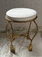 Full front view of round stool showing twisted gilt rope frame and tasseled feet under white cushion