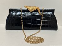 Front view of black croc clutch with gold-tone alligator clasp and chain strap