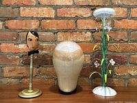 Photo showing all three hat stands against a brick wall background on a wooden surface.