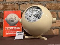 Front view of cream-colored Think Tank device with instruction booklet beside it