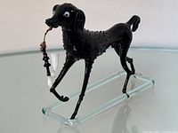 Full side view of the black Murano dog figurine showing the raised texturing on the body and clear glass base.