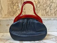Front view of navy blue leather handbag with red lucite handles on marble surface.