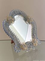 Angled view of mirror on wooden easel stand showing pale blue Murano glass frame with bead border and floral appliqués