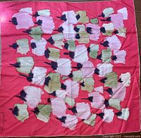 Full view of the square floral silk scarf with coral red background and various white and green flowers accented with black centers.