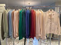 Full rack of 31 silk pussy bow blouses hung on chrome garment rack showing assorted solids and prints