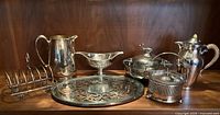 Full set of vintage silver plated serving pieces arranged on wooden shelf.