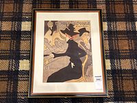 Framed poster print lying flat on a plaid carpet, showing full artwork with visible mat and frame.