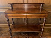 Front view of walnut server showing raised backsplash, two drawers, lower shelf and turned legs